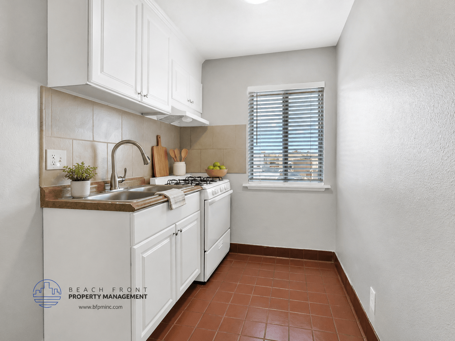 A kitchen with white cabinets and a brown tile floor.
